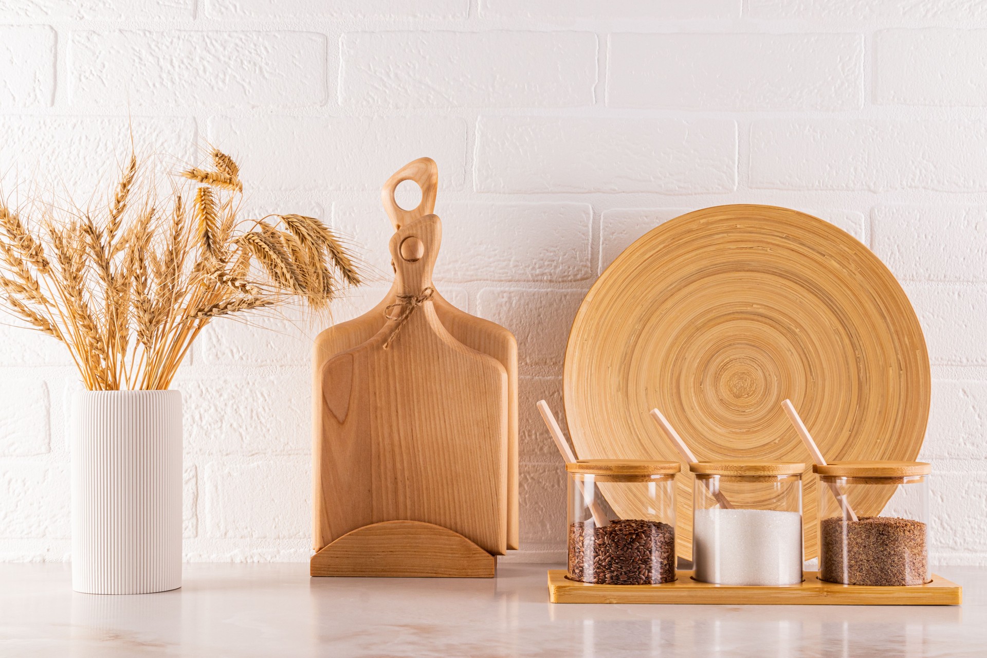 Stylish kitchen backdrop of modern spice storage area on marble countertop. wooden cutting boards, a bamboo dish, a vase with ears of wheat. eco style